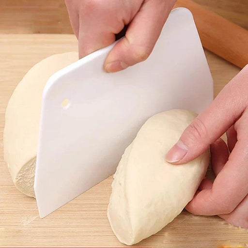 Hand using a white dough scraper to divide dough into portions on a wooden surface.