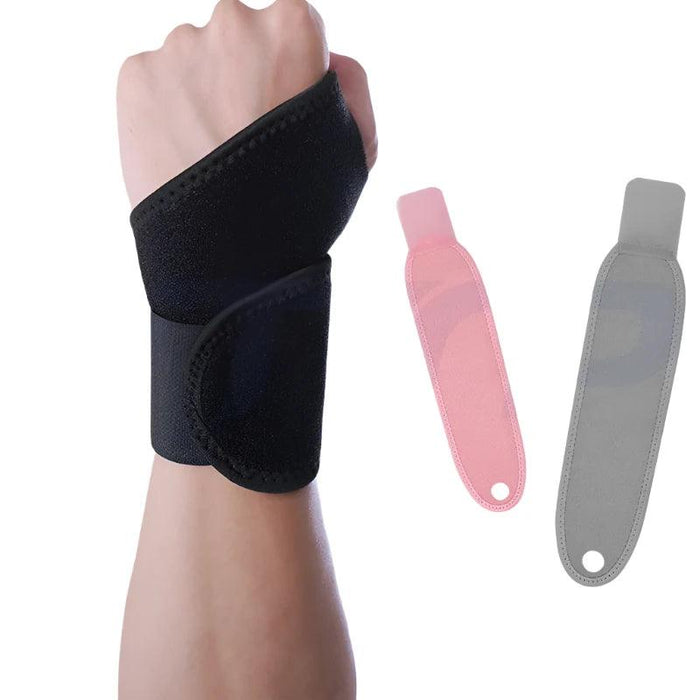 A hand wearing a black wrist support wrap. The wrap is made of a similar material as the pink one and is shown alongside two other wraps, one in pink and one in gray, which are laid flat.