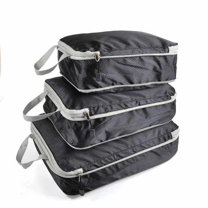 Three black packing cubes with gray zippers and handles, stacked on top of each other. Each cube has a zipper pull with a black tab.