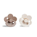 A brown, flower-shaped pacifier with a ring handle next to an ivory, flower-shaped pacifier with a ring handle.