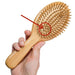 A hand holding an oval bamboo hairbrush with wooden bristles. A red arrow points to a small air hole in the center of the brush pad.