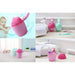 A collage showing pink and mint green baby rinse cups in different bathroom settings, used for holding toothbrushes and other bathroom items, along with a baby enjoying a bath with one of the cups.