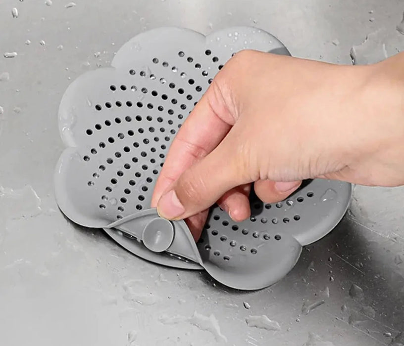 A hand removing a gray silicone drain cover with suction cups from a wet surface.