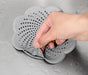 A hand removing a gray silicone drain cover with suction cups from a wet surface.