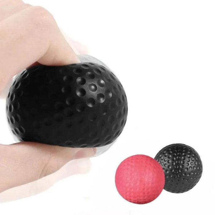 Close-up of a black textured reflex ball being squeezed, with red and black balls shown in the background, highlighting the ball's flexibility and grip.