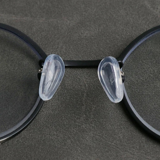 a close-up of a pair of eyeglasses with transparent silicone nose pads attached to the black frame, highlighting their soft and comfortable design.