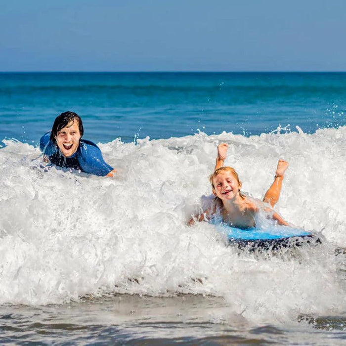 Two children riding waves on bodyboards, enjoying the ocean.