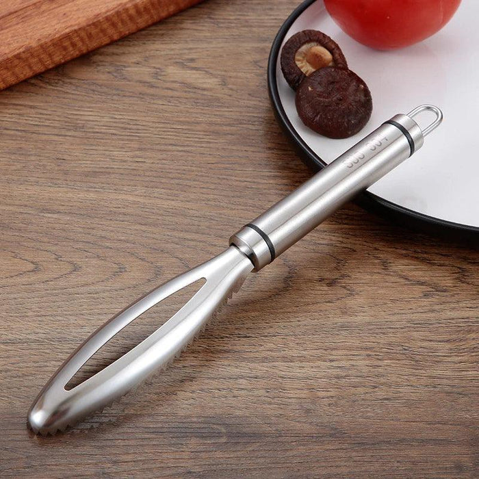 a stainless steel fish scaler with a serrated edge, placed on a wooden countertop beside a plate with mushrooms and a tomato.