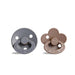 A round, gray pacifier with a ring handle next to a brown, flower-shaped pacifier with a similar ring handle.