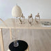 Three abstract sculptures in contemplation poses are arranged on a minimalist table next to a modern lamp.