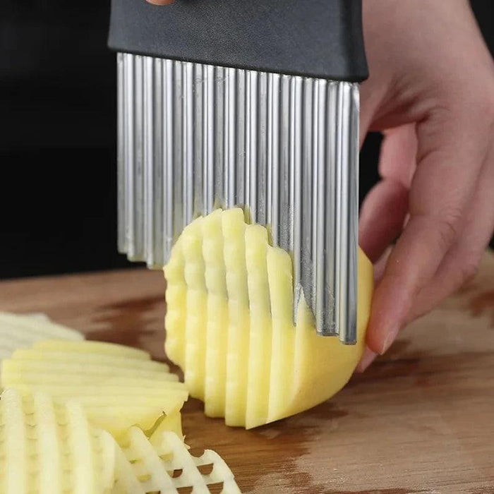 A person using a crinkle cutter to slice a potato on a wooden cutting board, demonstrating the tool's functionality in creating crinkle-cut vegetable slices.