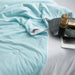 Light blue cooling blanket draped on a bed with decoration tools beside it.
