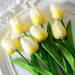 Artificial yellow and white tulips with green leaves on a decorative white plate.