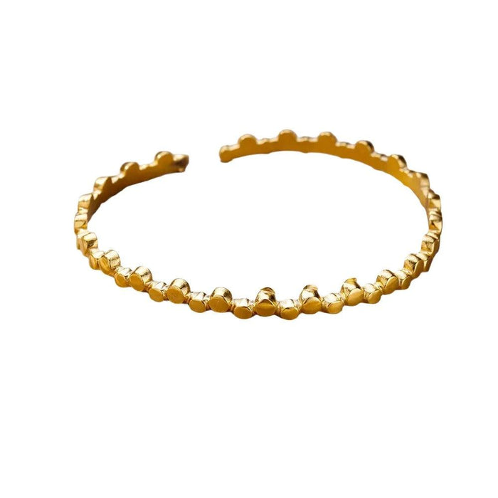 Gold cuff bracelet with a scalloped edge design, displayed on a white background.