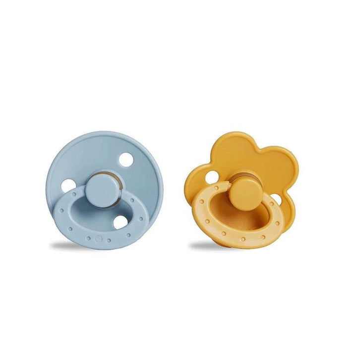 A round, blue pacifier with a ring handle next to a yellow, flower-shaped pacifier with a ring handle.