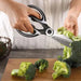 Close-up of multi-purpose kitchen scissors cutting broccoli on a wooden cutting board.