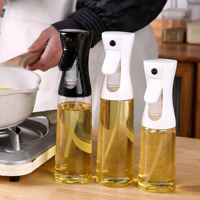 Three oil spray bottles in black and white variations, filled with oil, on a kitchen counter.