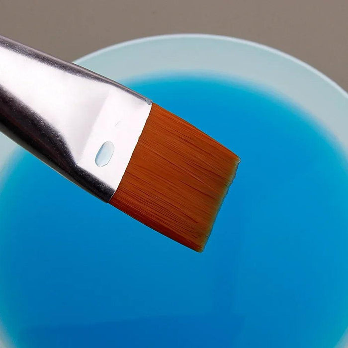 Close-up of a paintbrush with orange bristles dipped in a container of blue liquid.