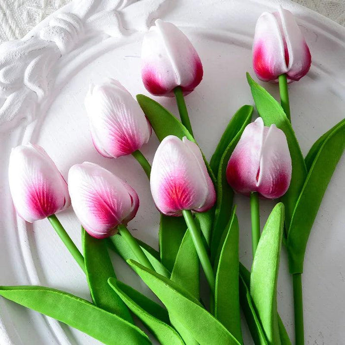 Artificial white and magenta tulips with green leaves on a decorative white plate.