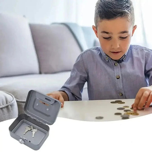 A young boy sorting coins on a table with a small grey lockbox open beside him, containing keys inside. The scene is set in a cozy living room.