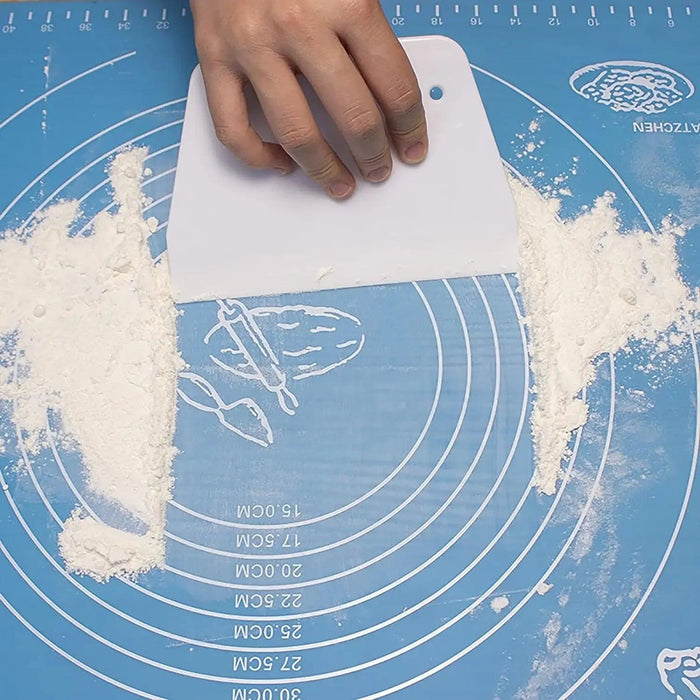 Hand holding a white dough scraper, cleaning flour off a blue pastry mat.