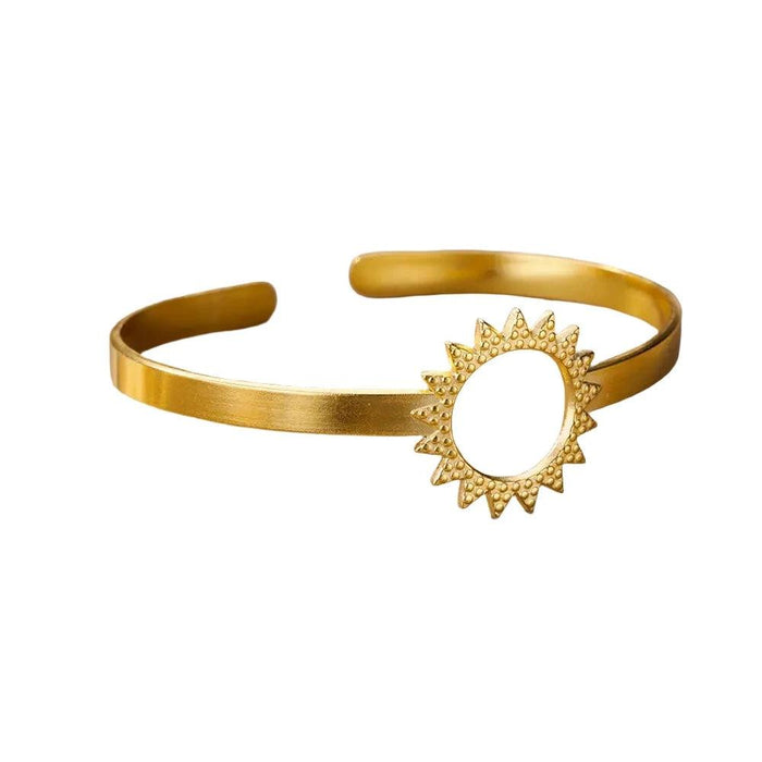 Gold cuff bracelet with a sunburst circle design, displayed on a white background.