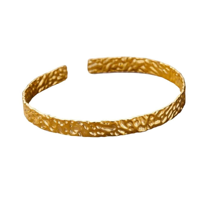 Thin gold cuff bracelet with a hammered texture, displayed on a white background.