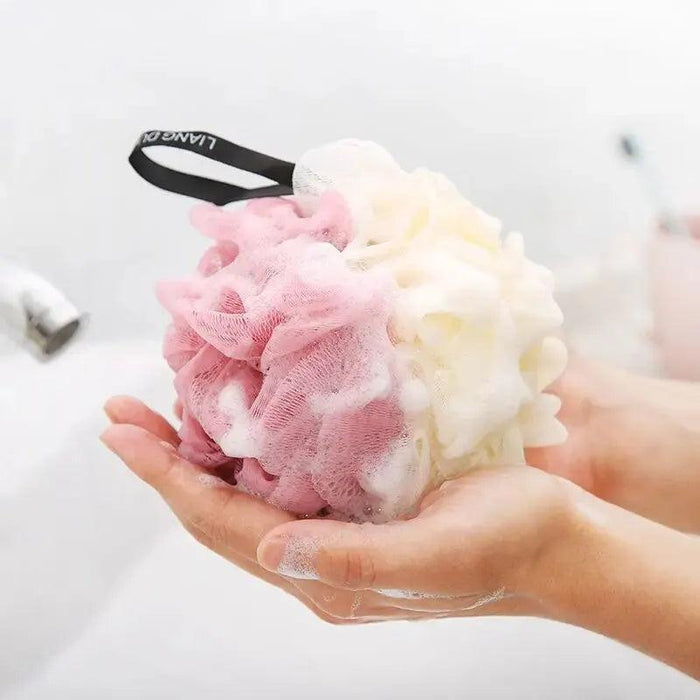 A close-up of a person's hands holding a pink and white bath loofah, creating a rich lather.