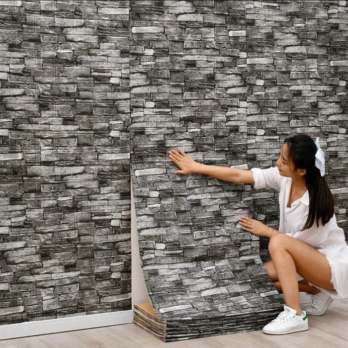 A person applying a wall panel with a stacked stone design in shades of dark gray.