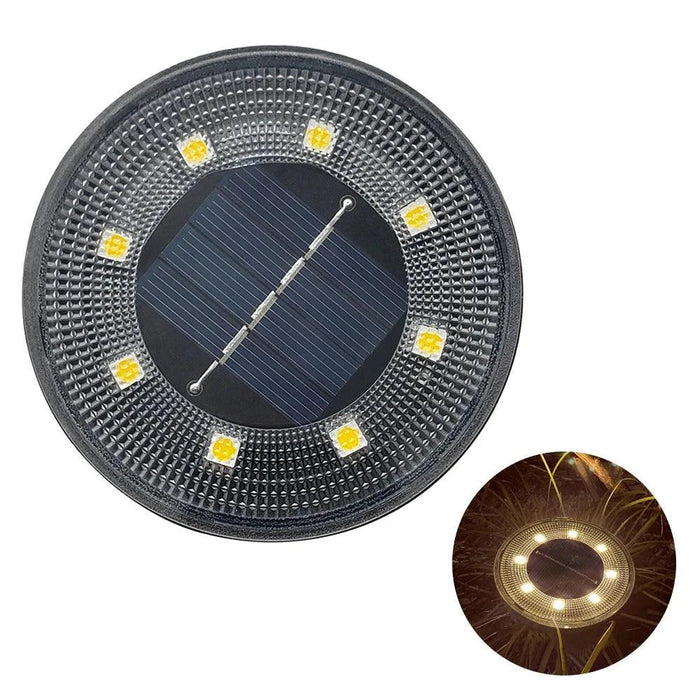 A close-up image of a round solar-powered garden light with a dark frame and multiple LED lights arranged in a circular pattern around a solar panel in the center. An inset shows the light illuminated at night, emitting a warm glow.