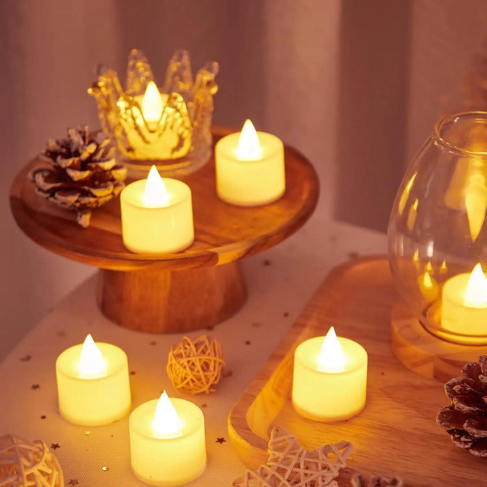 A rustic, warm setting with several white LED tea light candles placed on a wooden stand and surrounded by decorative items like pine cones and glass ornaments. The candles emit a soft yellow glow, enhancing the cozy and inviting atmosphere.