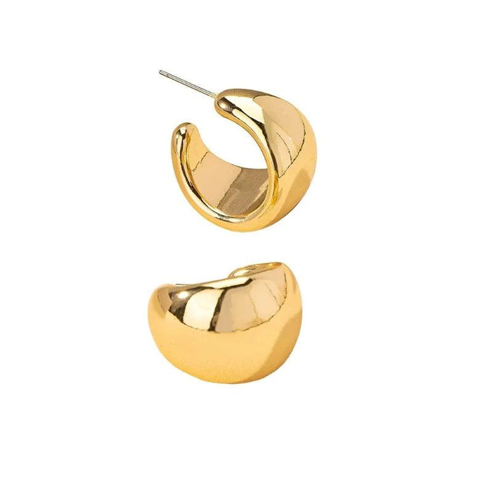 a pair of chunky, crescent-shaped gold earrings. These earrings are highly reflective, with a smooth surface, emphasizing their modern and bold design.