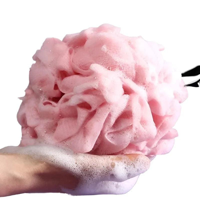 A close-up of a pink bath loofah being held in one hand, producing a thick foam.