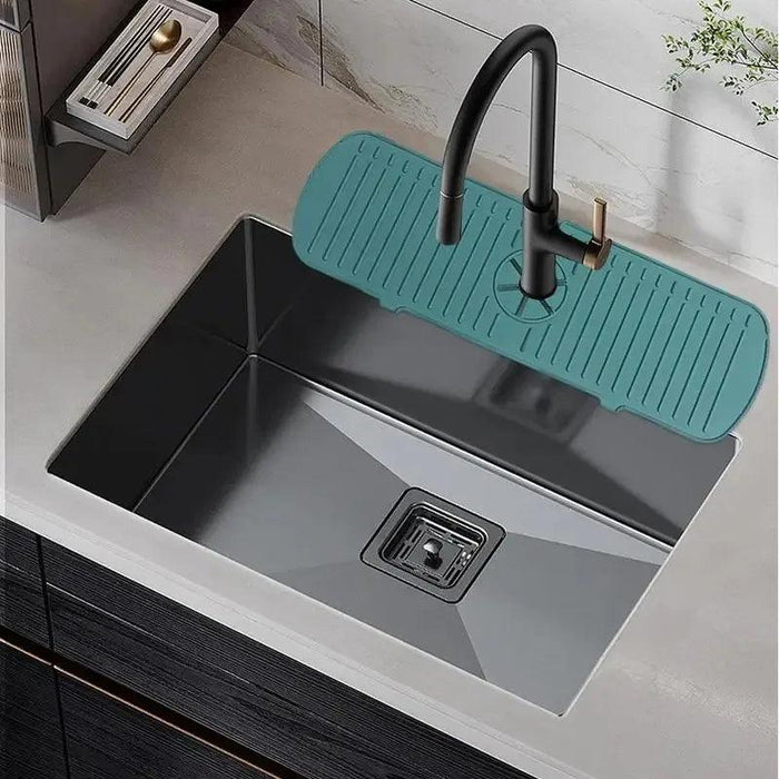 A teal-colored silicone splash guard is placed around the base of a faucet on a modern kitchen sink. The mat fits snugly around the faucet, demonstrating how it helps to keep water from splashing onto the countertop.