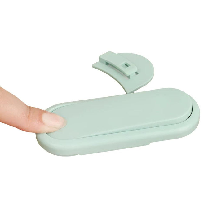 a mint green child safety lock being pressed down, demonstrating how it locks in place. The lock has a simple and sleek design, ensuring that it blends in with various home decor styles while providing safety.