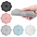 Five flower-shaped silicone drain covers in different colors, with a hand squeezing one of them to show flexibility.