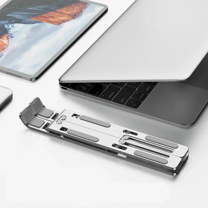 Silver adjustable laptop stand folded and placed next to a laptop and tablet, highlighting its portability.