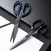 Two pairs of scissors, one with blue handles and one with black handles. They are displayed on a black surface with a white sheet, emphasizing their sharp blades and ergonomic handles.