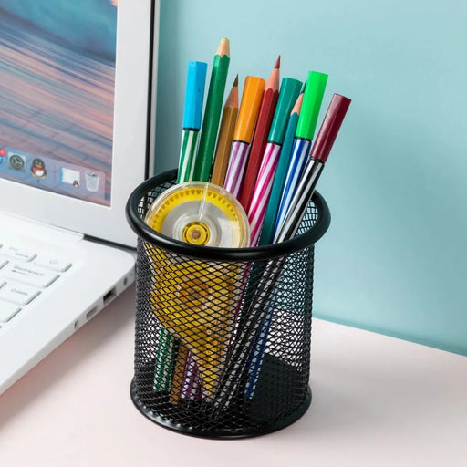 Round black mesh pen holder filled with colorful pens and a yellow correction tape, placed next to a laptop.