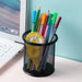 Round black mesh pen holder filled with colorful pens and a yellow correction tape, placed next to a laptop.