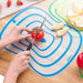  slicing a tomato on the blue-circled cutting mat, demonstrating its use as a chopping board. The mat is placed on a wooden table, with additional mats and cut fruits visible in the background.