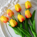 A bouquet of yellow tulips with red tips and green leaves on a white plate.