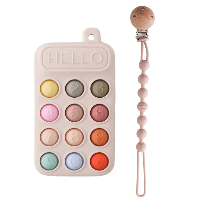 A beige silicone teether resembling a phone keypad with colorful buttons, next to a pacifier clip with a wooden clasp and pink silicone beads.