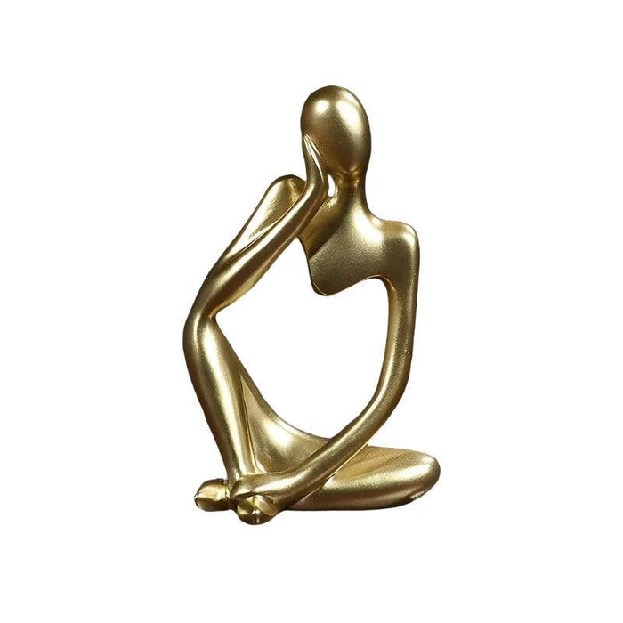 Gold minimalist abstract sculpture of a figure sitting cross-legged with one arm resting on the head.