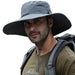 Man wearing a wide-brimmed gray sun hat while hiking, with a backpack on his shoulders. The hat provides sun protection, perfect for outdoor activities such as hiking and camping.