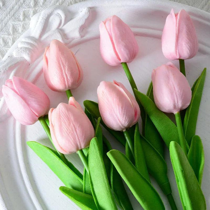 A bouquet of bright pink tulips with green leaves on a white plate.