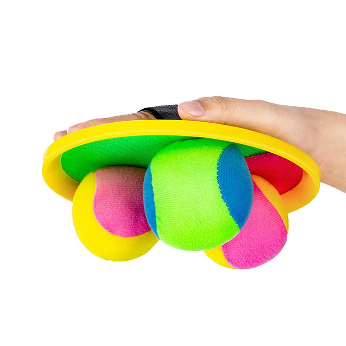 Hand holding a Velcro catch paddle with multiple colorful balls attached.