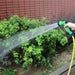 A person using the green garden hose nozzle to water plants in a garden.