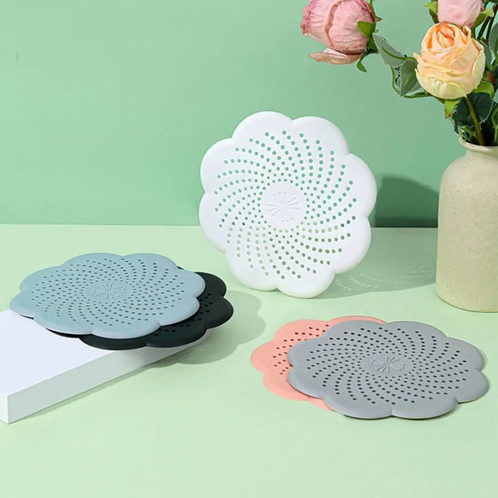 Multiple flower-shaped silicone drain covers displayed on a green background, with some lying flat and others standing upright.