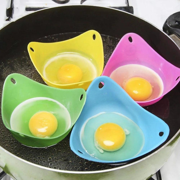 A close-up view of four silicone egg poachers in green, blue, yellow, and pink, each holding an egg, floating in boiling water inside a pan.